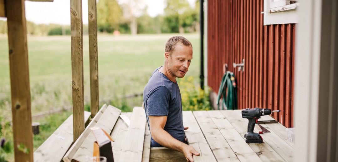 Ein Mann arbeitet an der Holzterrasse eines roten Schwedenhauses. 