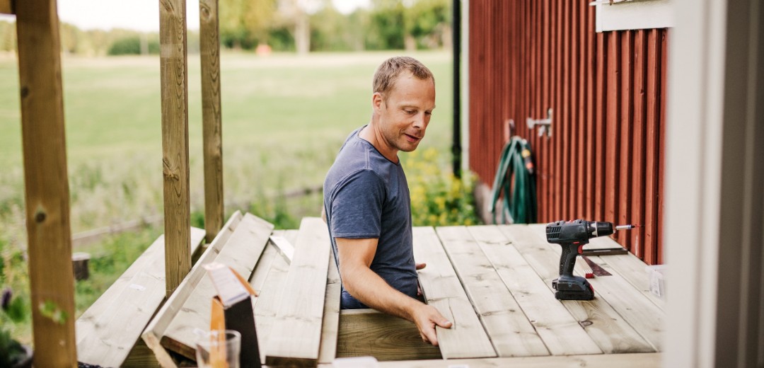 Ein Mann arbeitet an der Holzterrasse eines roten Schwedenhauses. 