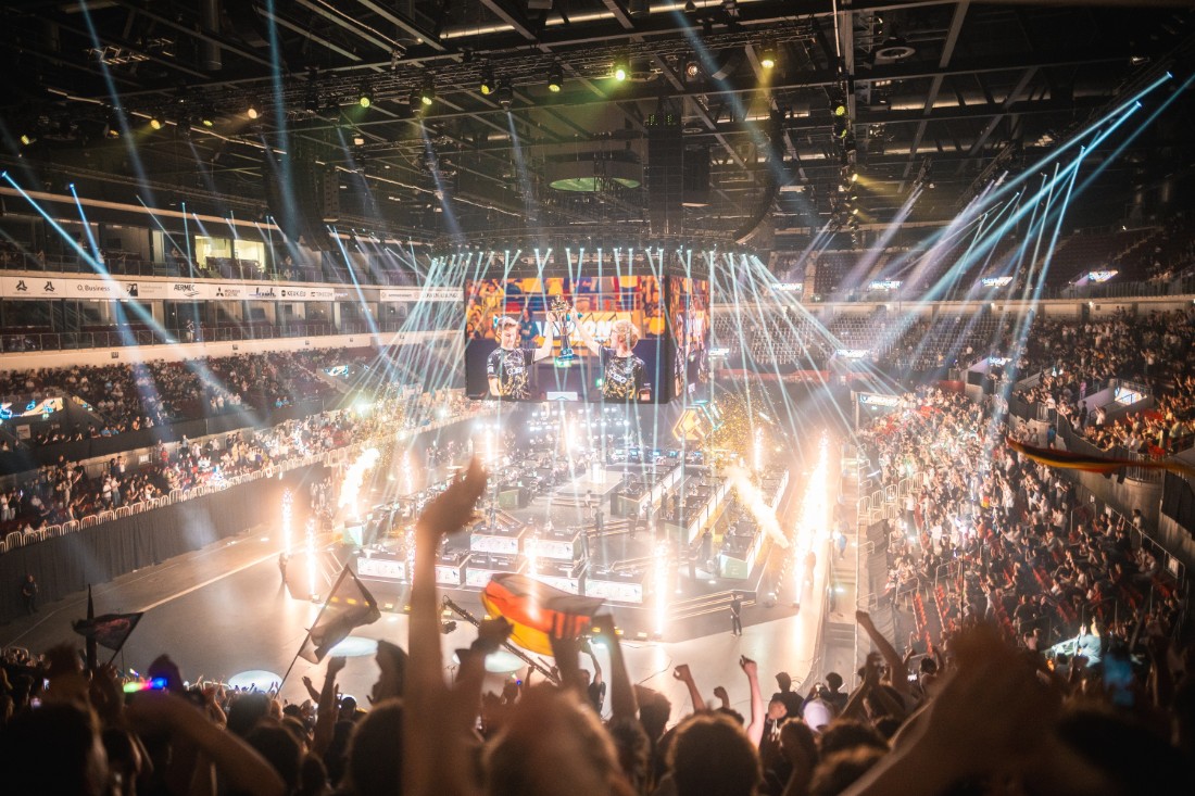 Große BIG E-Sport-Arena mit jubelndem Publikum, Lichtshow, Bühne und Spielstationen während eines Turniers.