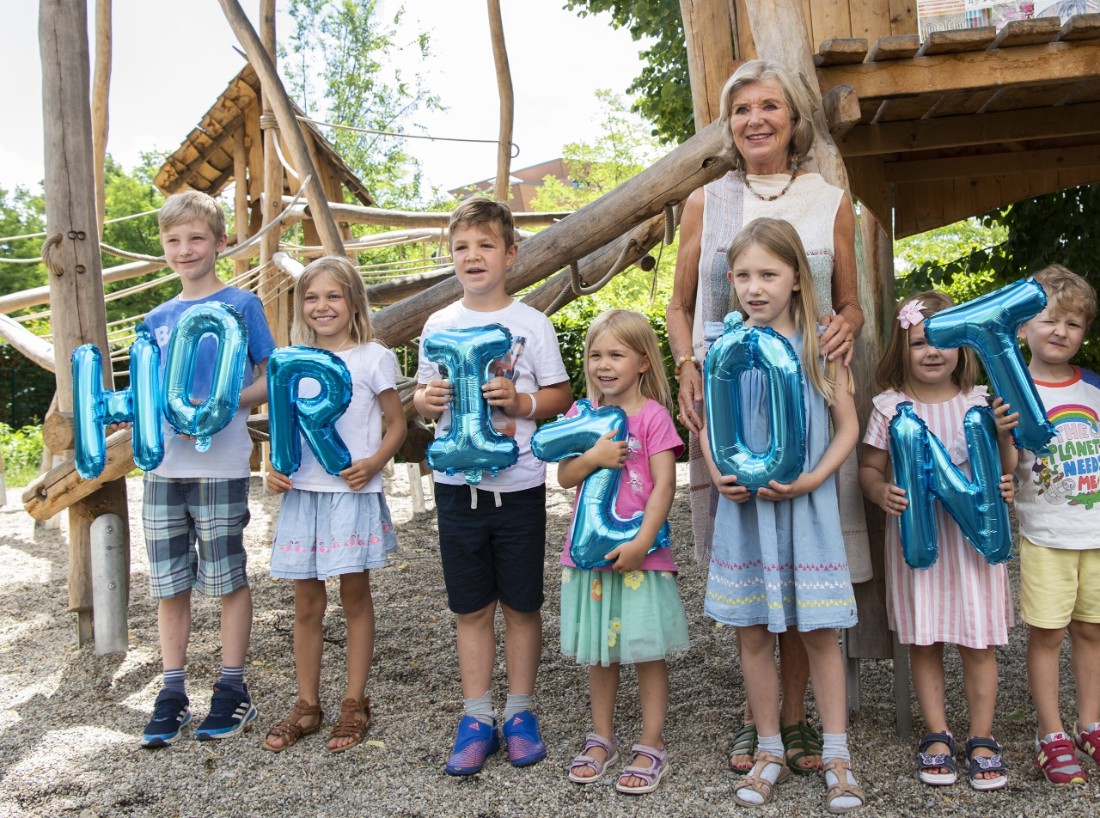 Kinder mit blauen Ballonbuchstaben "HORIZONT" auf einem Spielplatz, neben ihnen Gründerin Jutta Speidel.