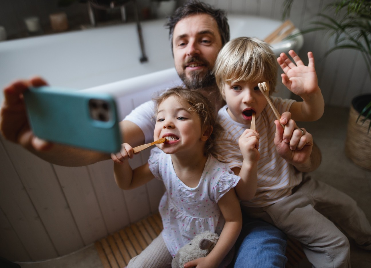 Ein Vater nimmt mit seiner Tochter und seinem Sohn ein Selfie auf, während sie beide am Zähne putzen sind. Ein Vater nimmt mit seiner Tochter und seinem Sohn ein Selfie auf, während sie beide am Zähne putzen sind.