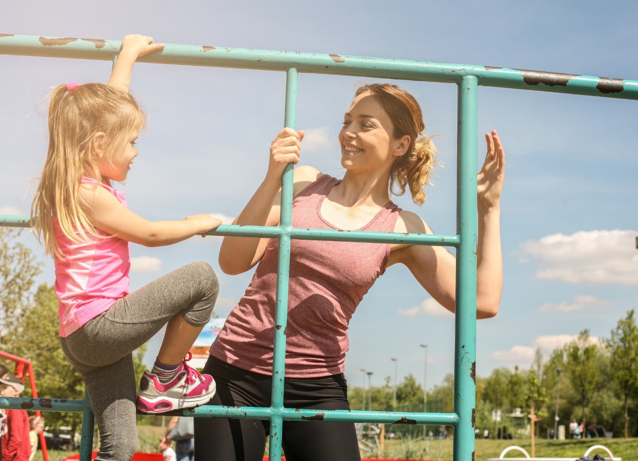 Bühnenbild Ratgeber kindersicherer Sommer Ein Kind klettert gemeinsam mit ihrer Mutter in Sportklamotten ein Klettergerüst entlang.