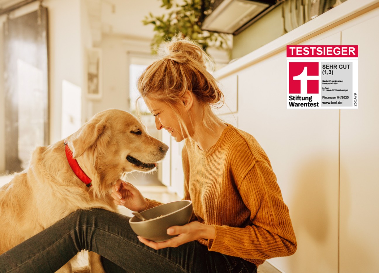 Junge Frau sitzt in der Küche auf dem Boden und füttert ihren Hund mit Testsieger-Siegel mit der Note 1,3