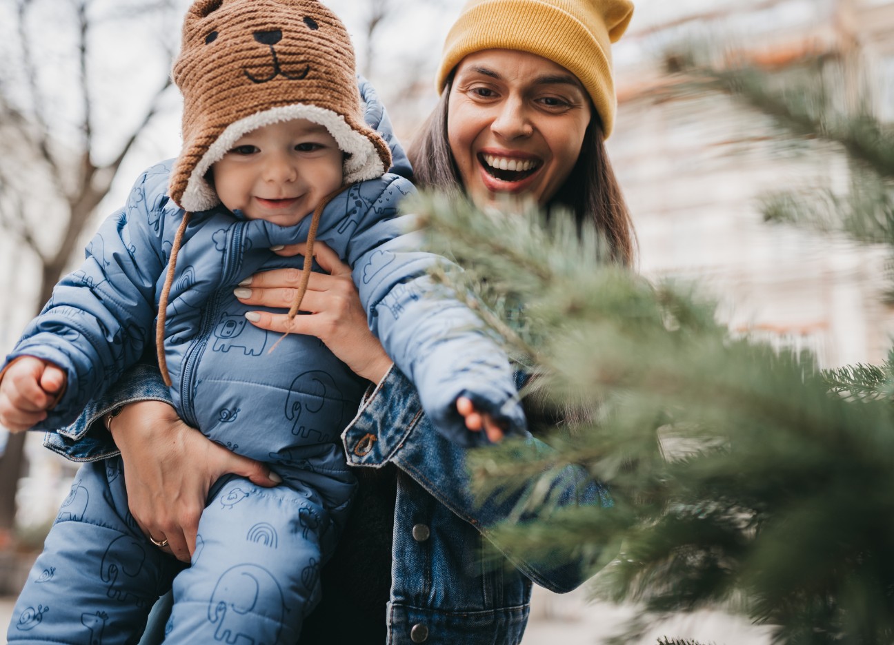 Bühnenbild Ratgeber finanzielle Absicherung als Geschenk zur Geburt des Kindes Glückliche Frau hält ihr Baby vor einem Tannenbaum.