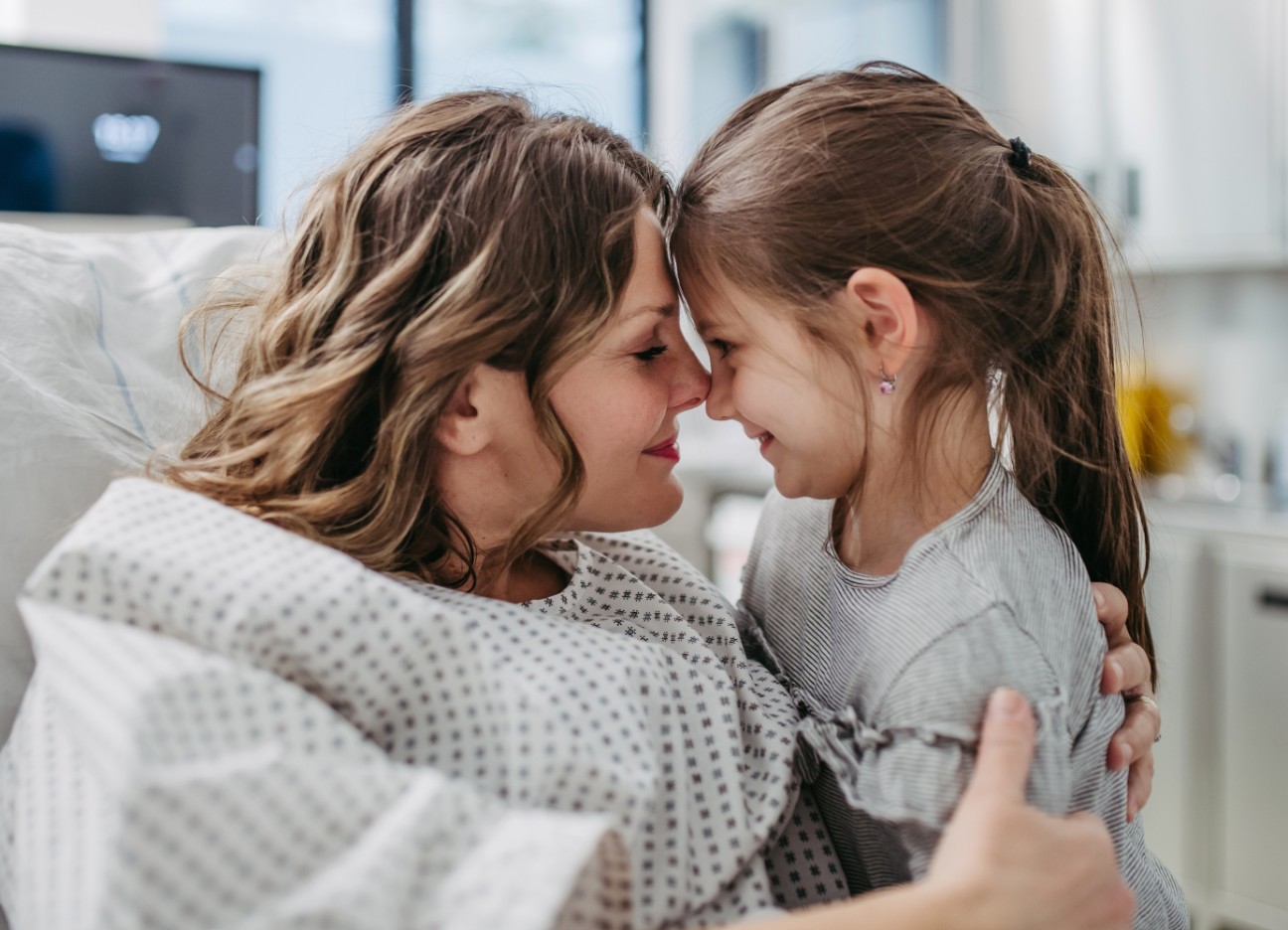 Eine Frau im Krankenbett und ihre kleine Tochter geben sich einen Nasenkuss Eine Frau im Krankenbett und ihre kleine Tochter geben sich einen Nasenkuss