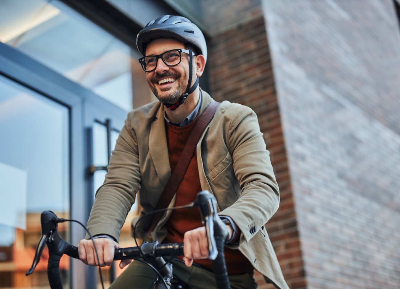 Bühnenbild Produktseite Fahrradversicherung Ein Mann im Sacko mit Helm fährt mit seinem Fahrrad los.
