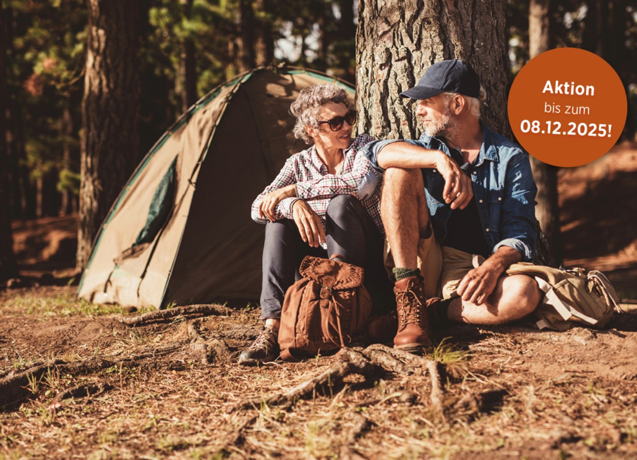 Eine Frau ein Mann in Wanderkleidung sitzen nebeneinander angelehnt an einen Baum und unterhalten sich. Hinweis im Bild: Aktion bis zum 08.12.2025
