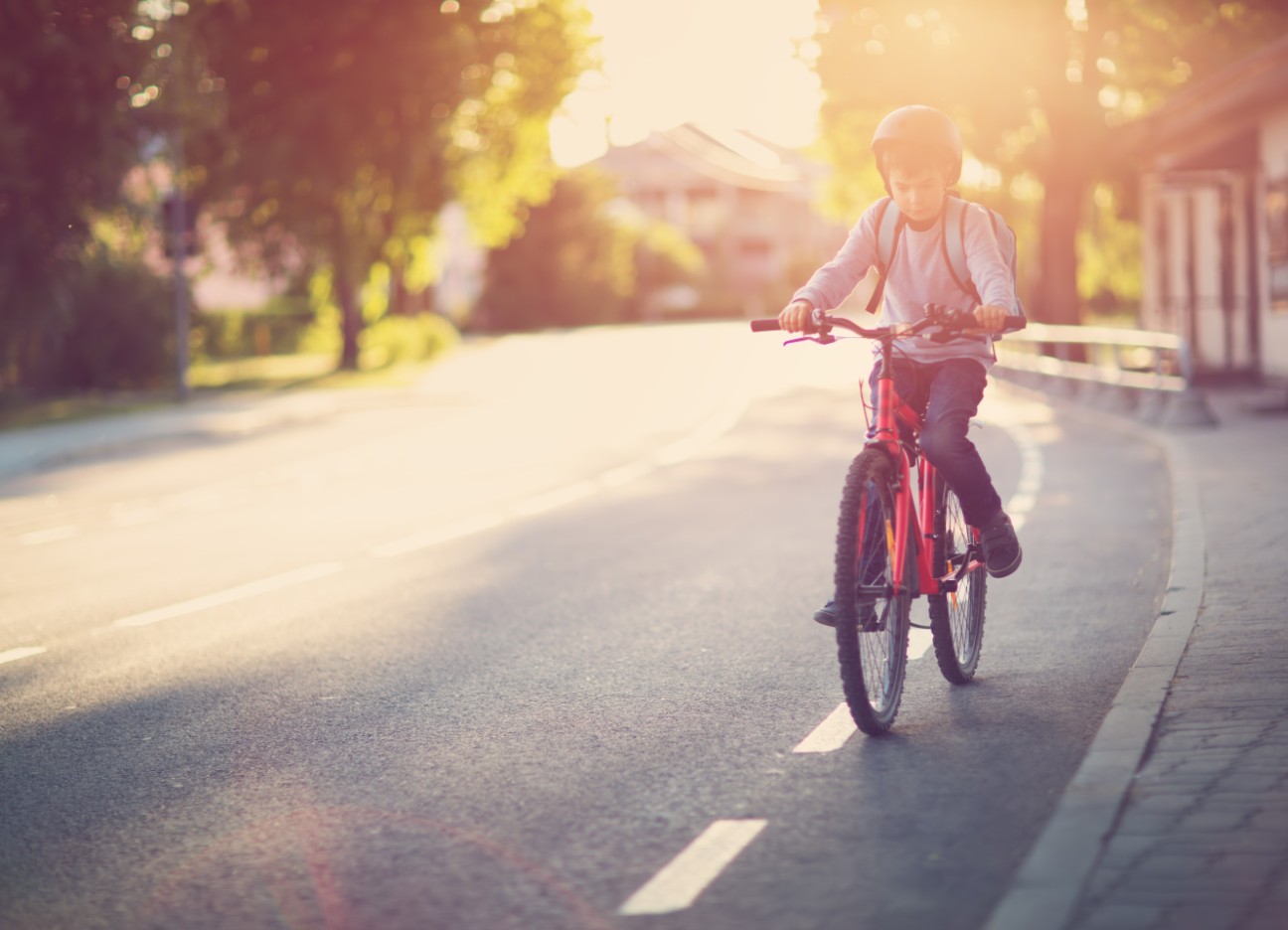 Bühnenbild Ratgeber Einschulung Schulweg Ein junges Kind fährt mit seinem Fahrrad den Fahrradstreifen auf einer Straße entlang.