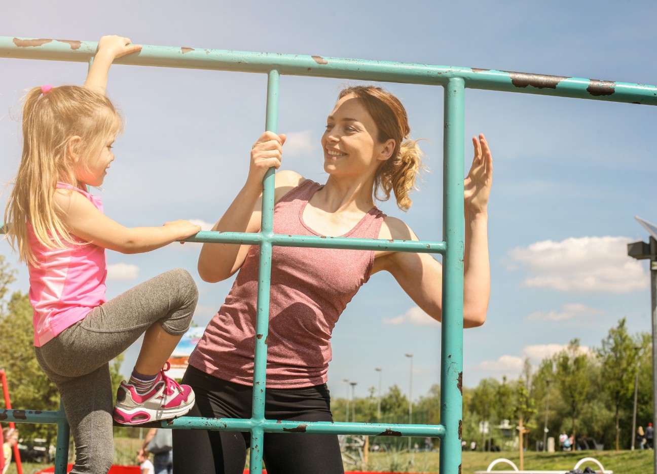 Bühnenbild Ratgeber kindersicherer Sommer Ein Kind klettert gemeinsam mit ihrer Mutter in Sportklamotten ein Klettergerüst entlang.
