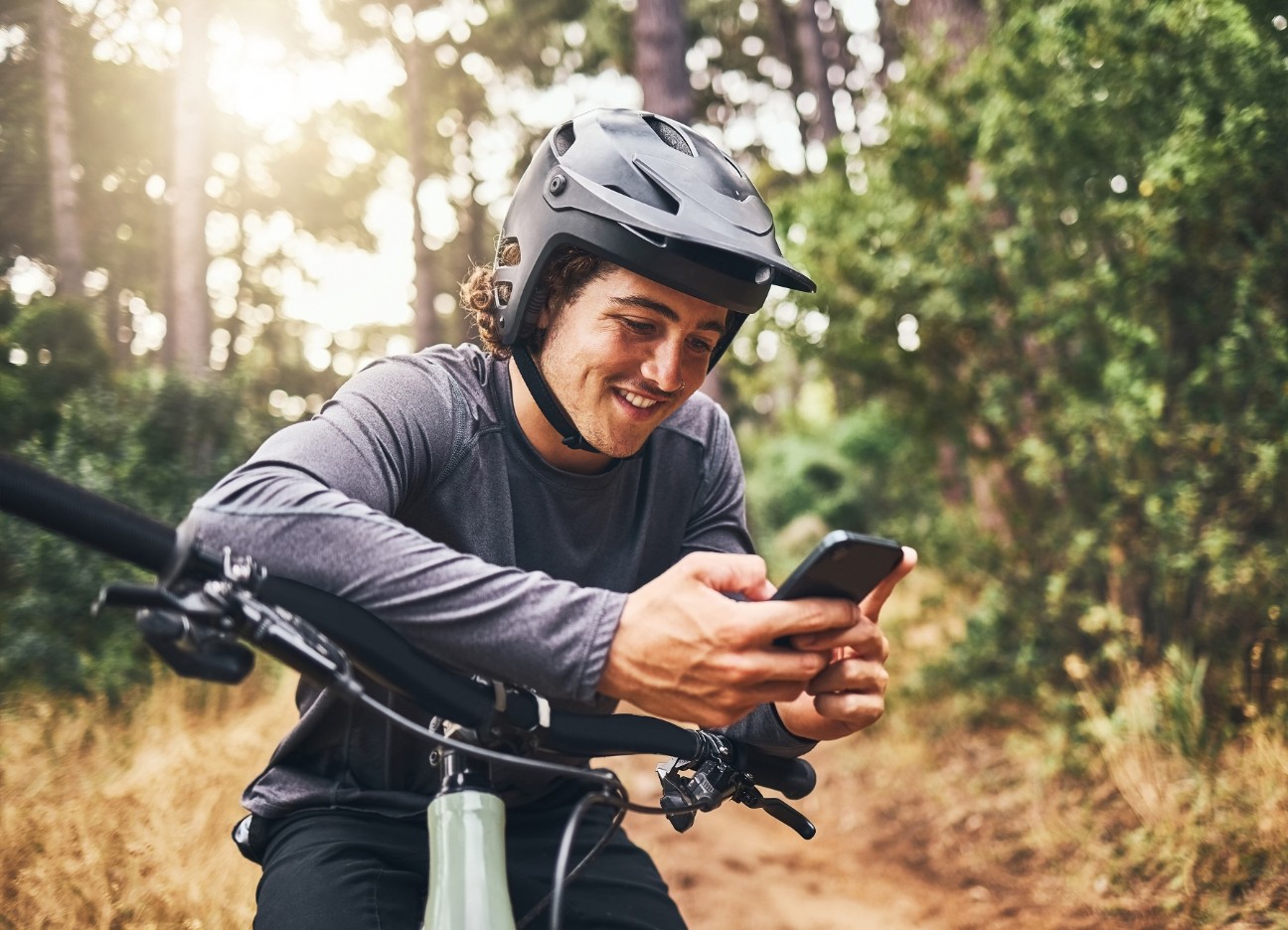 Junger Mann mit Helm und Smartphone auf seinem Mountainbike in der Natur Junger Mann mit Helm und Smartphone auf seinem Mountainbike in der Natur