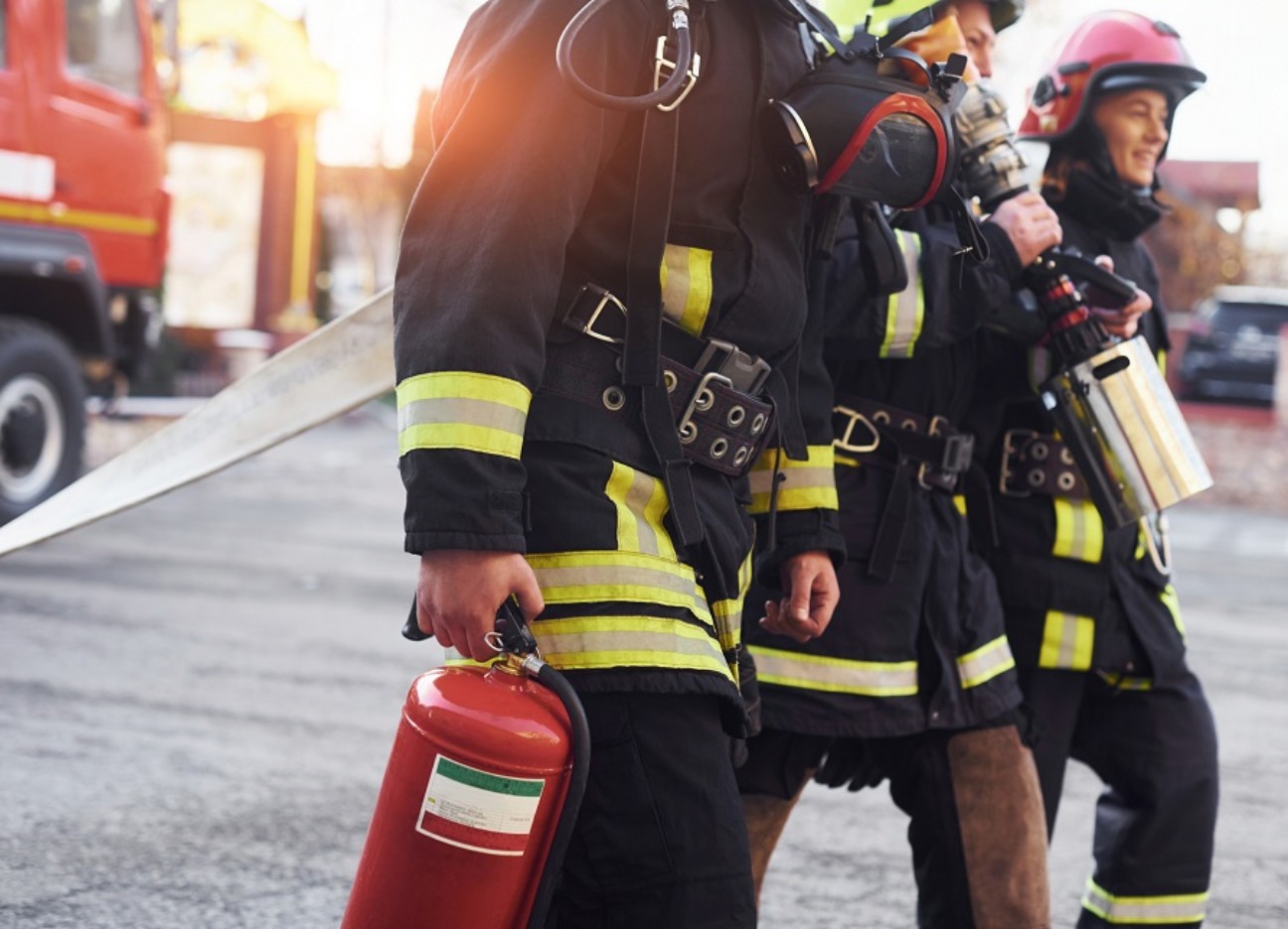 Bühnenbild Ratgeber Berufswunsch Feuerwehrmann Drei Feuerwehrleute laufen mit Equipment herum. Ihre Uniformen und Equipment stehen im Fokus des Bildes.