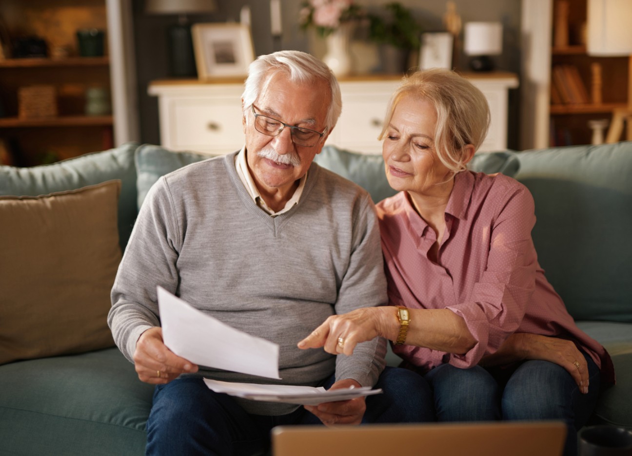 Älteres Paar sitzt auf dem Sofa und schaut gemeinsam Dokumente durch.