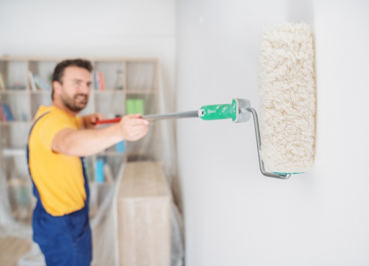 Ein Mann streicht eine Wand im Wohnzimmer mit weißer Farbe.