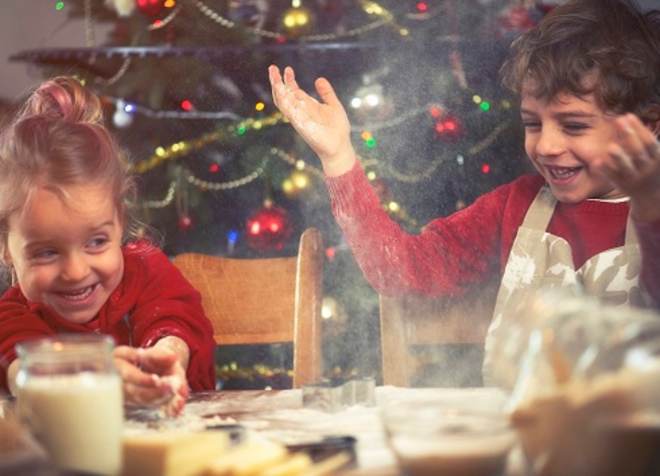 Bühnenbild Ratgeber Weihnachtsbaeckerei Zwei kleine Kinder backen zusammen und albern rum. Im Hintergrund ist ein Weihnachtsbaum.