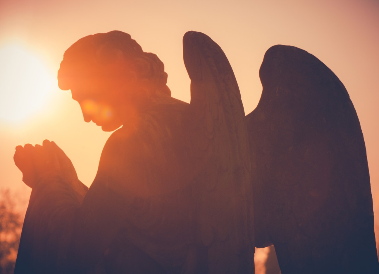 Im Sonnenuntergang steht eine Engelsstatue. 