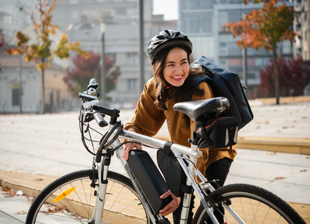 Eine junge Frau mit Rucksack und Fahrradhelm hockt vor ihrem E-Bike.