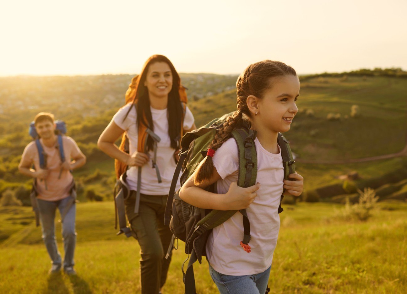 Eine junge Familie geht im Sonnenschein wandern. Die junge Tochter steht im Vordergrund.