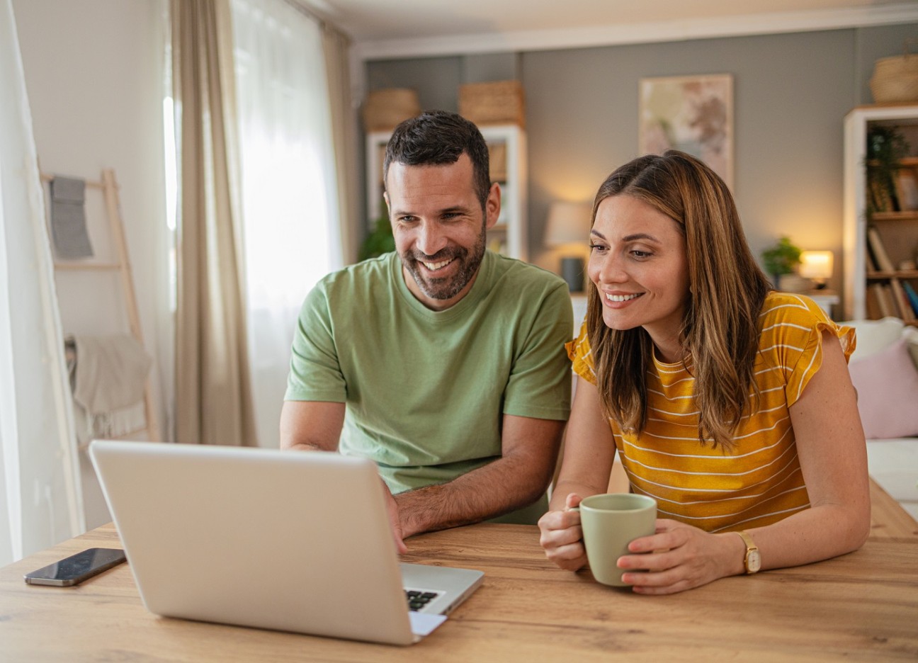 Ein Pärchen sitzt am Wohnzimmertisch und schaut gemeinsam auf einen Laptop.