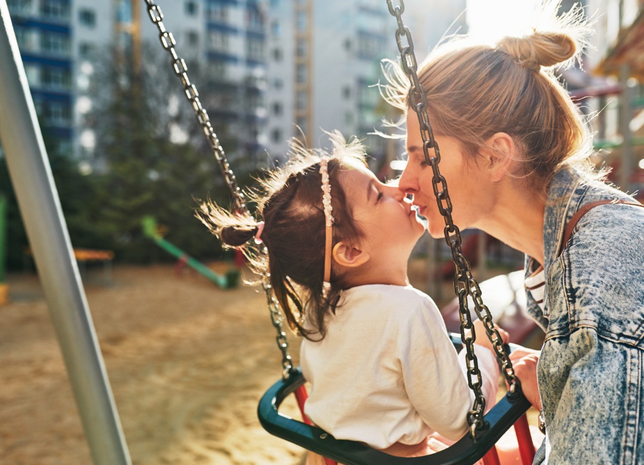Bühnenbild Ratgeber Kinderschutz Eine Mutter küsst ihr kleines Kind, welches in einer Schaukel sitzt.