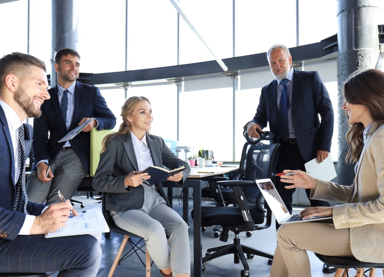 Fünfköpfiges Team bespricht sich in einem hellem Bürogebäude