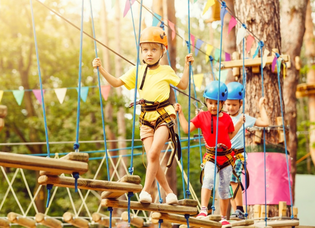 Mehrere Kinder laufen von Station zu Station in einem Kletterpark. 