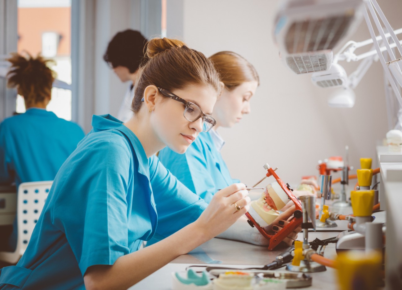 Bühnenbild Ratgeber Zahnersatz im Ausland Eine Zahnarzthelferin sitzt in einem Labor und arbeitet an einem Gebissmodell.