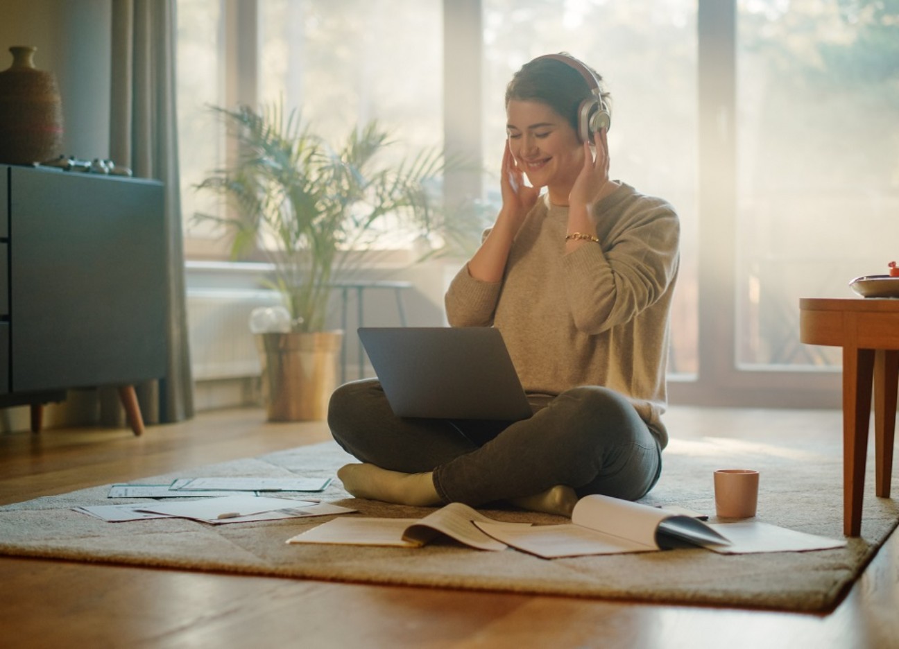 Junge Frau, die Laptop zu Hause benutzt, Remote-Arbeit macht, Musik über Kopfhörer hört. Junge Frau, die Laptop zu Hause benutzt, Remote-Arbeit macht, Musik über Kopfhörer hört.