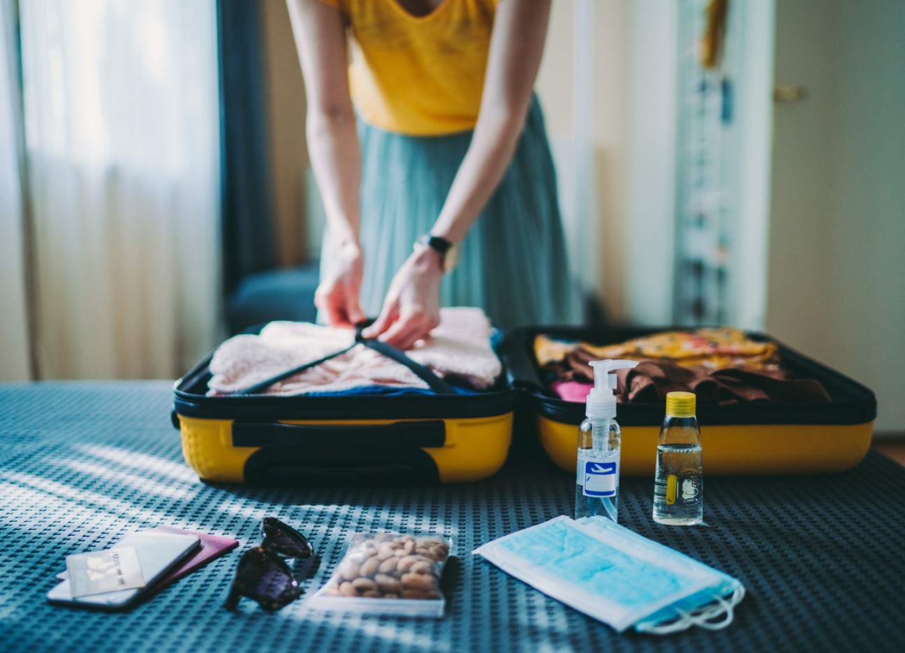 Bühnenbild Ratgeber Reiseapotheke Eine Frau packt ihren Koffer auf dem Bett und hat Medikamente für die Reiseapotheke bereitgelegt.