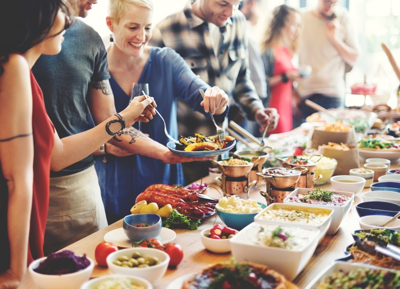 Mehrere Menschen stehen an einem vielseitigen, vollen Buffet.