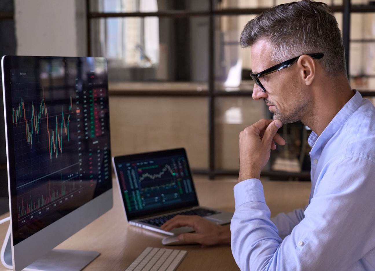 Bühnenbild Ratgeber Investieren in Kryptowährungen Ein Business-Mann sitzt im Büro am Computer und schaut sich Datenanalysen an.