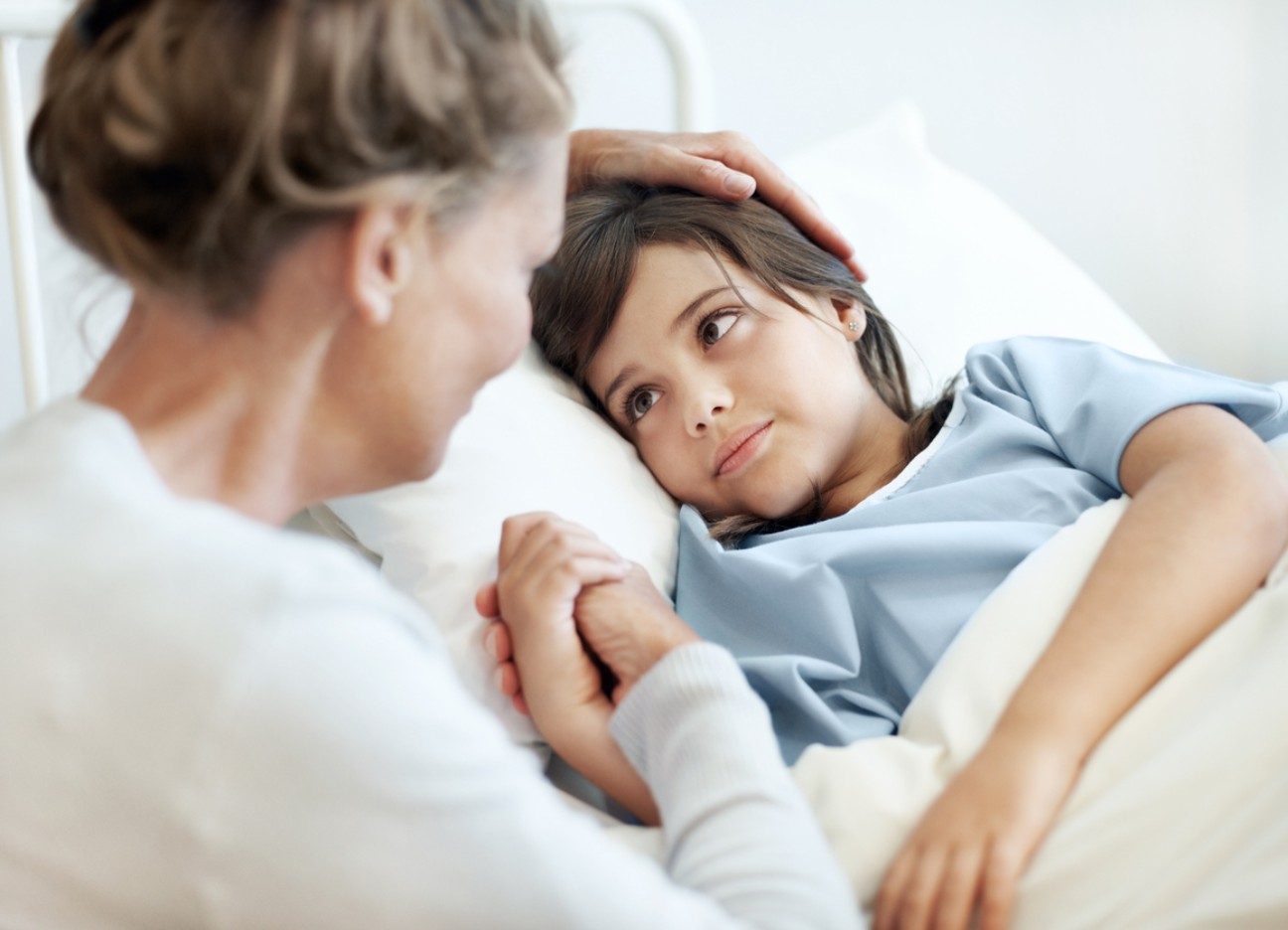 Ein kleiner Junge liegt im Krankenbett. Seine Mutter sitzt daneben und streichelt ihm den Kopf. Ein kleiner Junge liegt im Krankenbett. Seine Mutter sitzt daneben und streichelt ihm den Kopf.