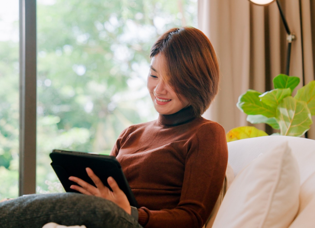 Eine Frau sitzt entspannt auf dem Sofa und schaut auf ihr Tablet Eine Frau sitzt entspannt auf dem Sofa und schaut auf ihr Tablet