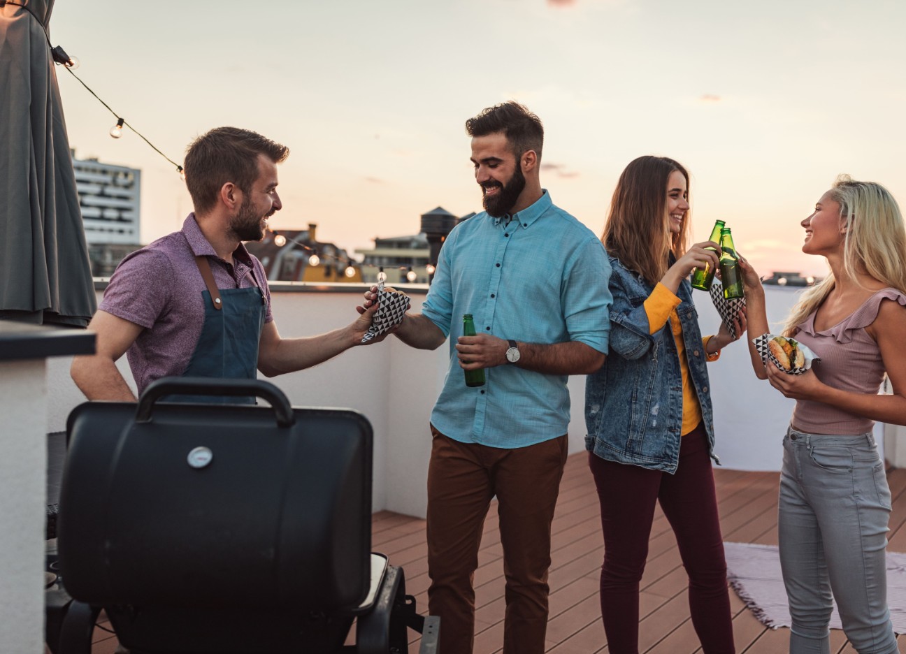 Bühnenbild Ratgeber Nachbarschaft Eine Gruppe von Leuten grillt zusammen auf einer Dachterrasse.