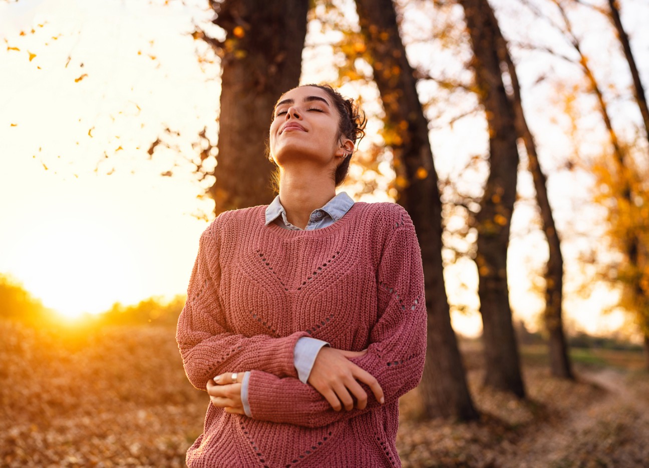 Frau genießt frische Luft im herbstlichen Wald bei Sonnenuntergang.