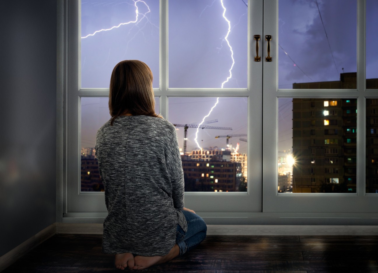 Bühnenbild Ratgeber Unwetter und Blitzableiter Ein Mädchen sitzt knieend an einem Fenster und schaut die sichtbaren Blitze in der Ferne an.
