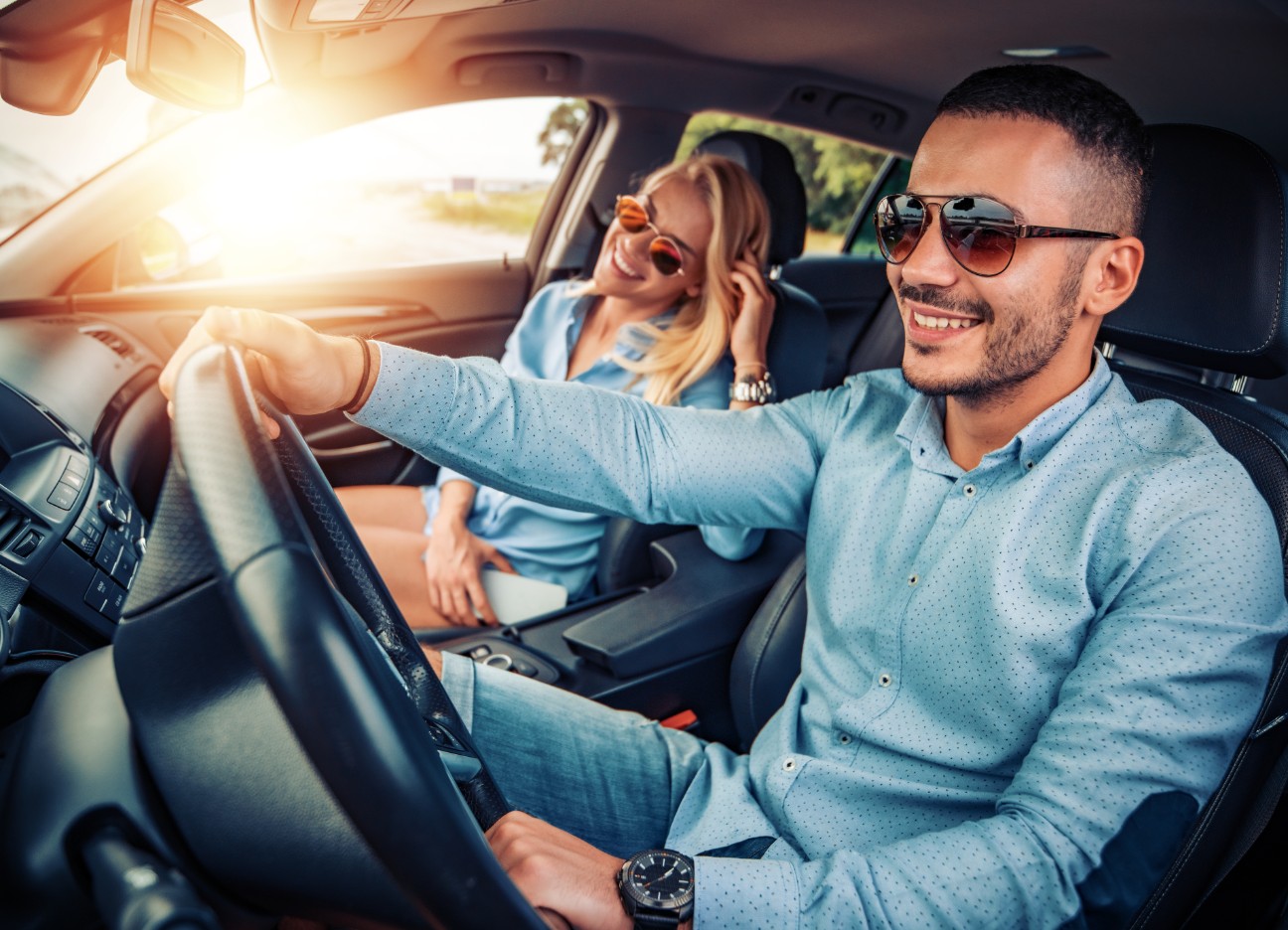 Junges Pärchen sitzt zusammen im Auto, während der Mann fährt Junges Pärchen sitzt zusammen im Auto, während der Mann fährt