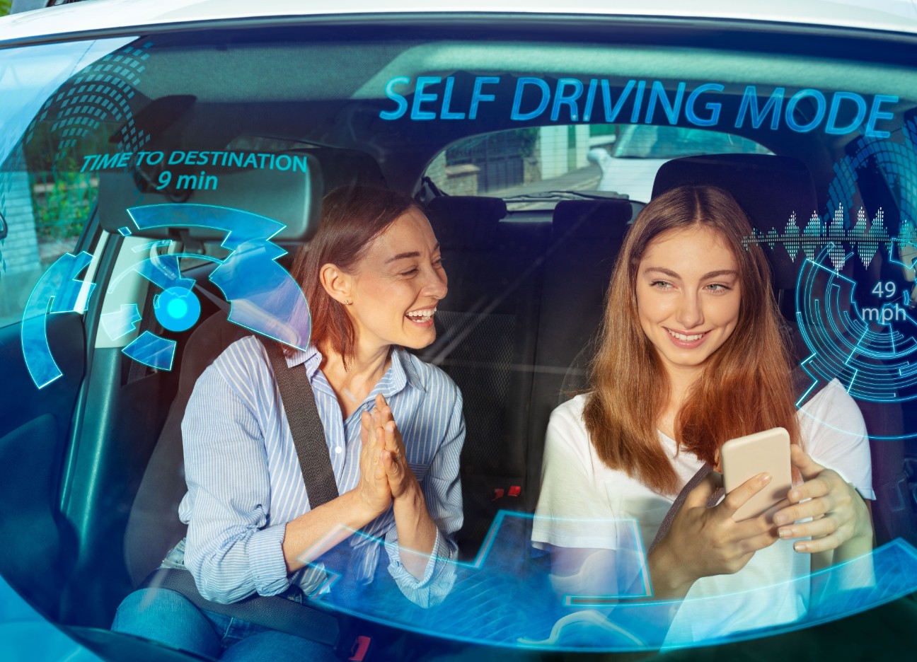 Bühnenbild Ratgeber Autonomes Fahren Zwei Freundinnen sitzen zusammen vorne im Auto und schauen in ein Smartphone.