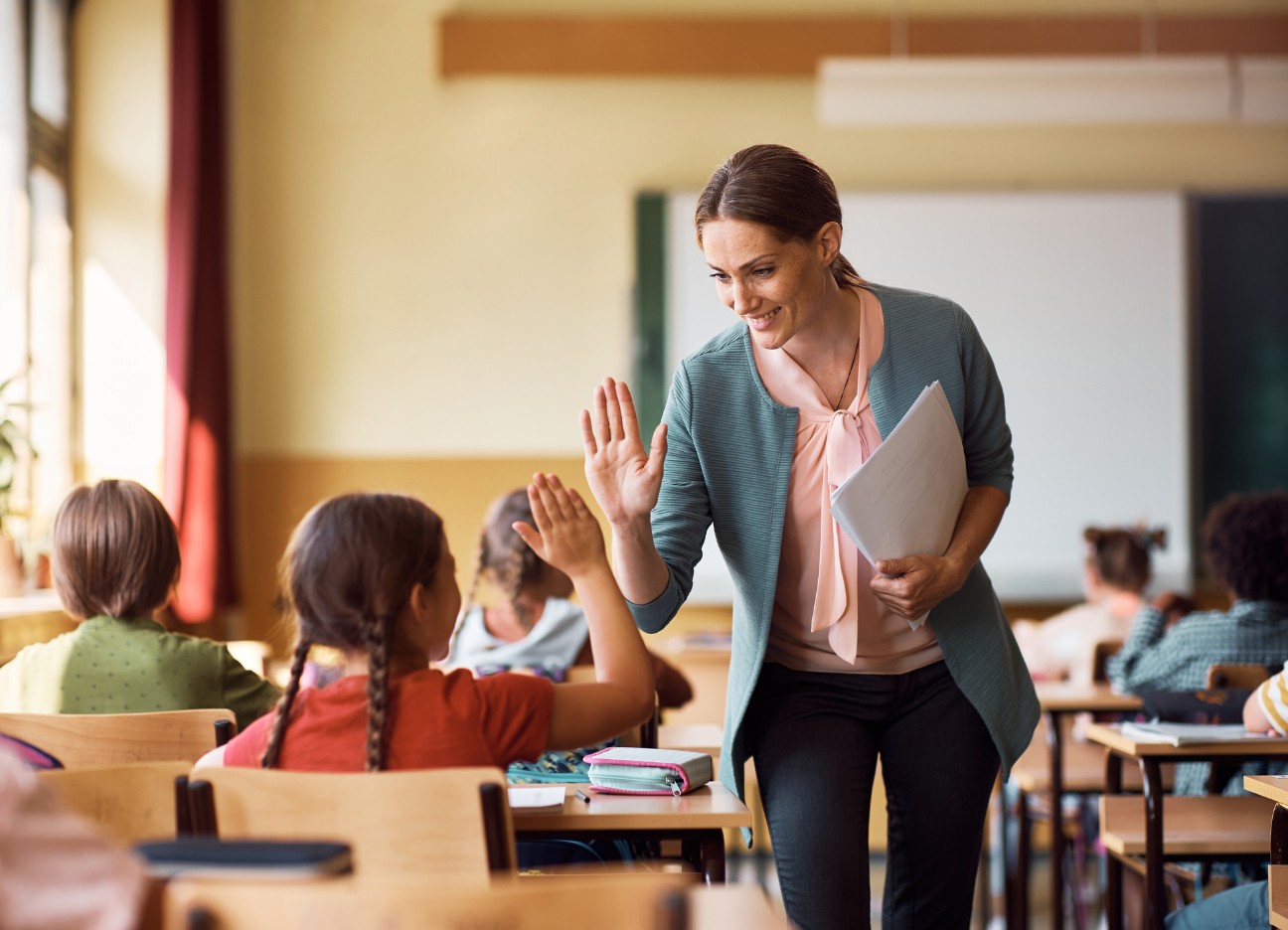 Eine Lehrerin läuft durch ihre Klasse und gibt einer Schülerin ein "high five" Eine Lehrerin läuft durch ihre Klasse und gibt einer Schülerin ein "high five"