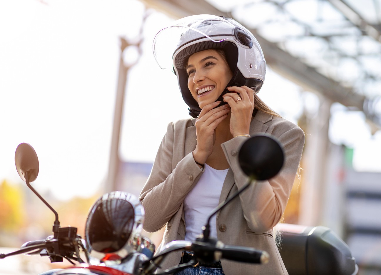 Eine junge Frau sitzt im Sonnenschein auf ihrem Moped-Roller und startet diesen.