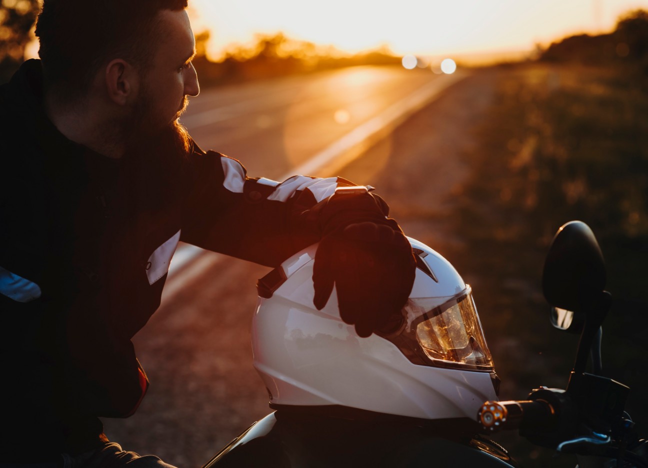 Motorradfahrer macht während einer Fahrt bei Sonnenuntergang eine Pause. Der Helm liegt auf dem Motorrad.