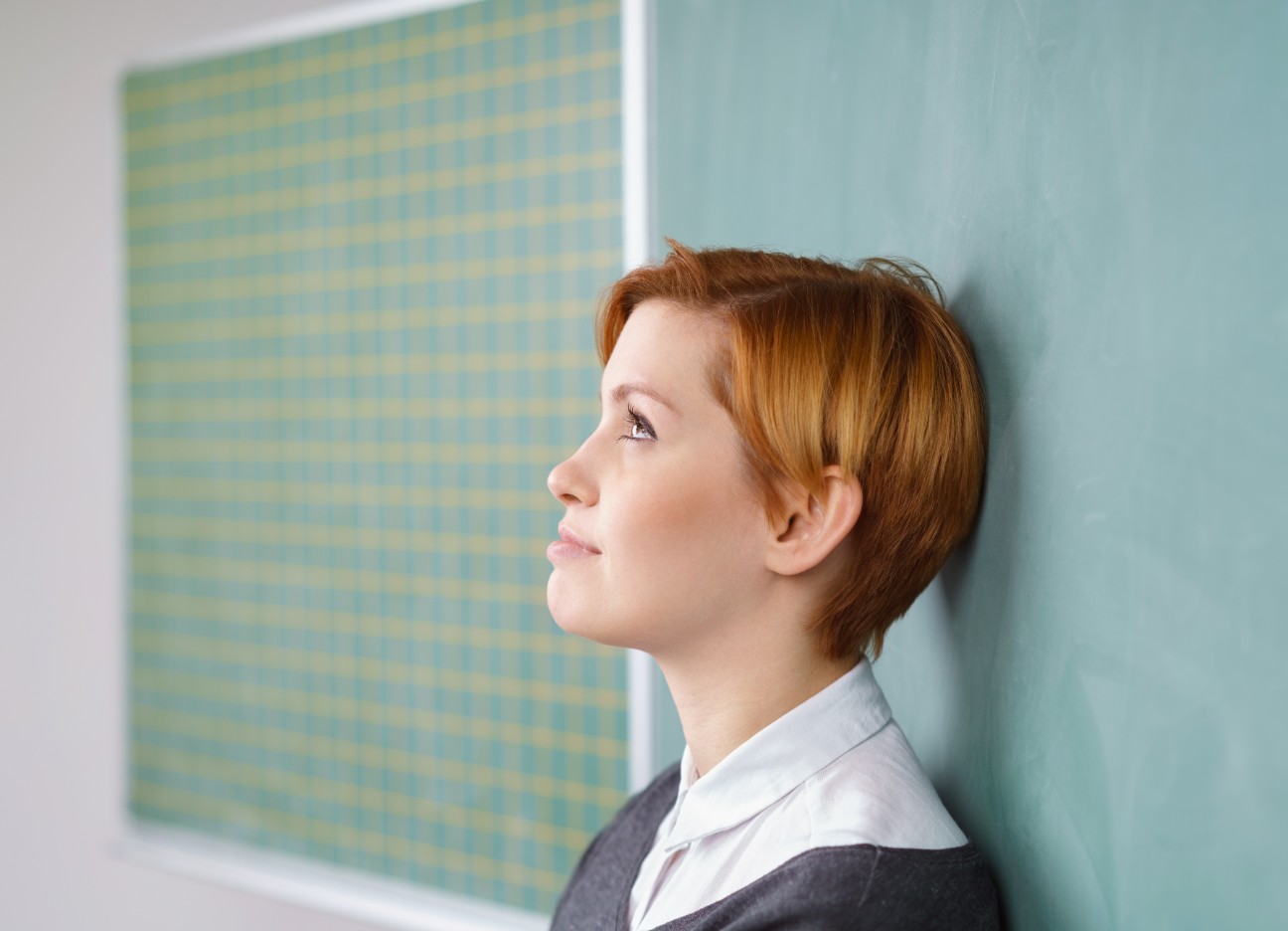 Eine Lehrerin lehnt ihren Kopf an die Tafel und schaut nachdenklich. 
