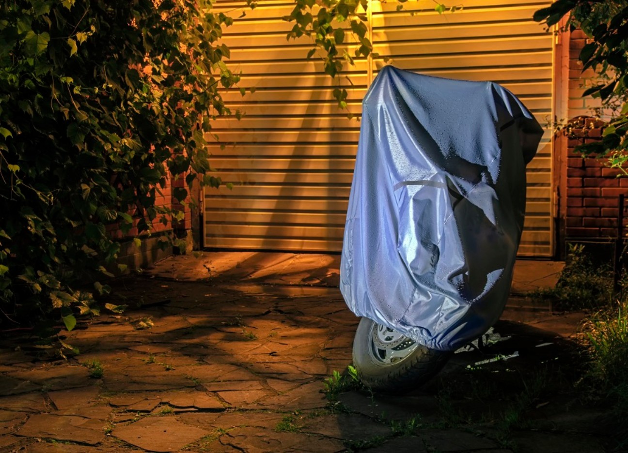 Ein überdecktes Motorrad steht im Dunkeln in der Auffahrt eines Hauses.