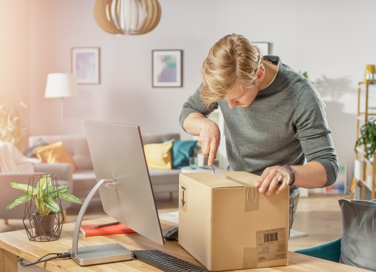 Bühnenbild Ratgeber Plagiate Ein Mann öffnet ein großes Paket, welches auf seinem Schreibtisch liegt.