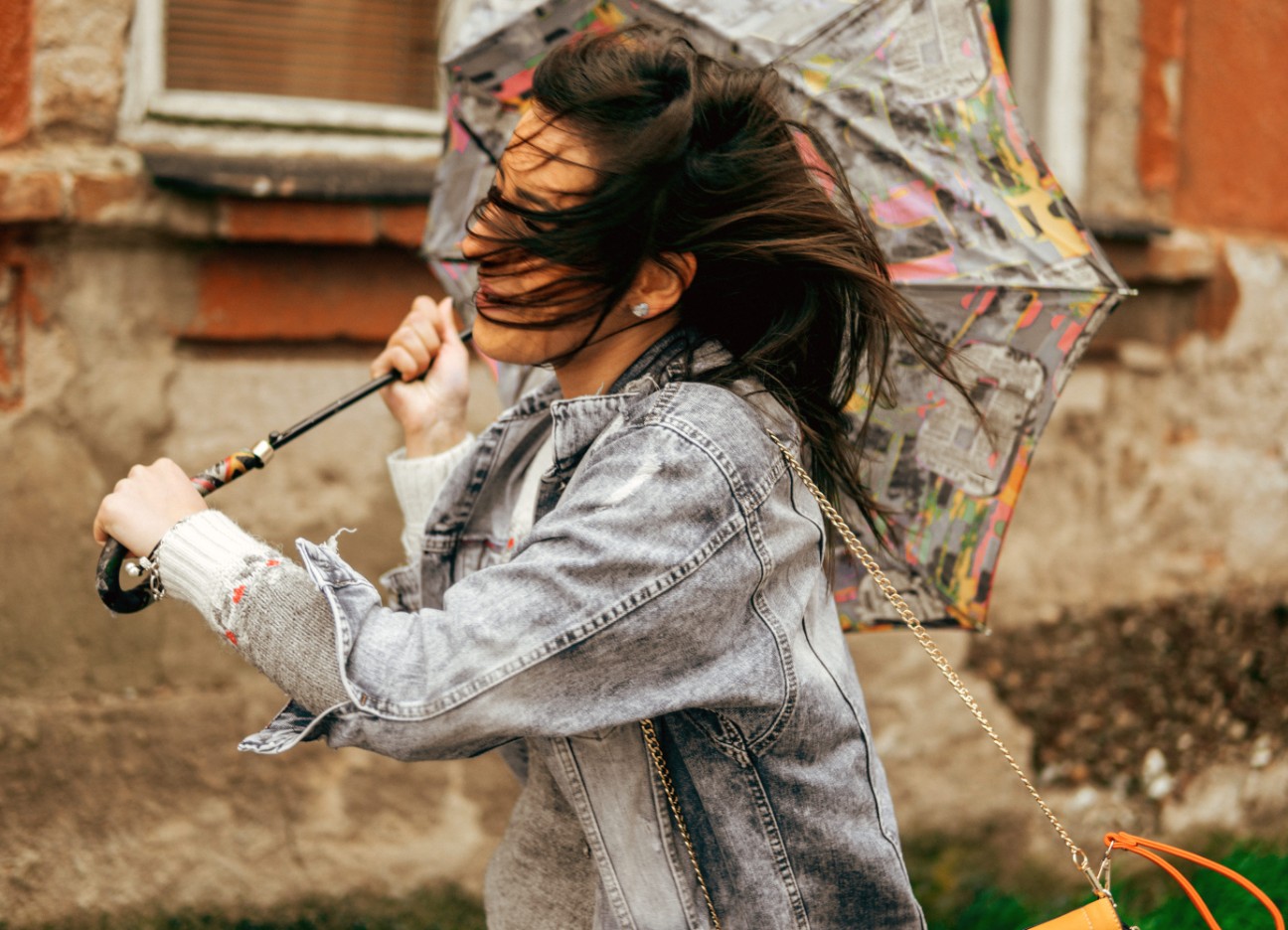 Bühnenbild Ratgeber Sturm und Gewitter Eine Frau läuft mit ihrem Regenschirm durch einen starken Wind. Der Regenschirm hat sich bereits umgedreht.