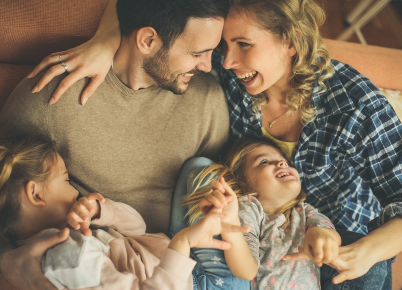 Bühnenbild Ratgeber Versicherungen junge Familien Ein junger Mann und eine junge Frau liegen Arm in Arm. Zwei junge Mädchen liegen auf ihren Schößen.