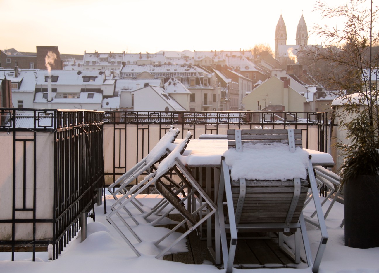 Das Bild zeigt einen Balkon mit Möbeln, die verschneit sind. 