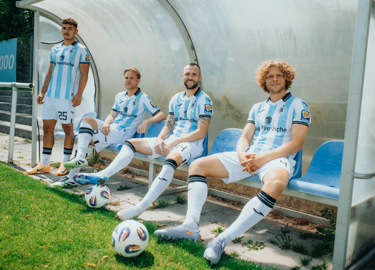 Vier TSV 1860-Fußballer sitzen im Trikot auf der Fanbank