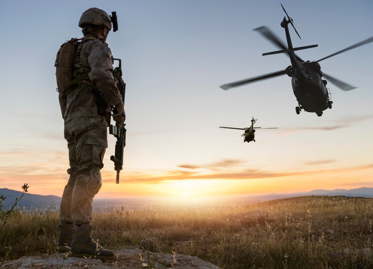 Bühnenbild Ratgeber Traumberuf Soldat: Tipps zur Karriere bei der Bundeswehr Ein Soldat steht bewaffnet auf einem Hügel schaut in Richtung wegfliegender Militärhubschrauber.