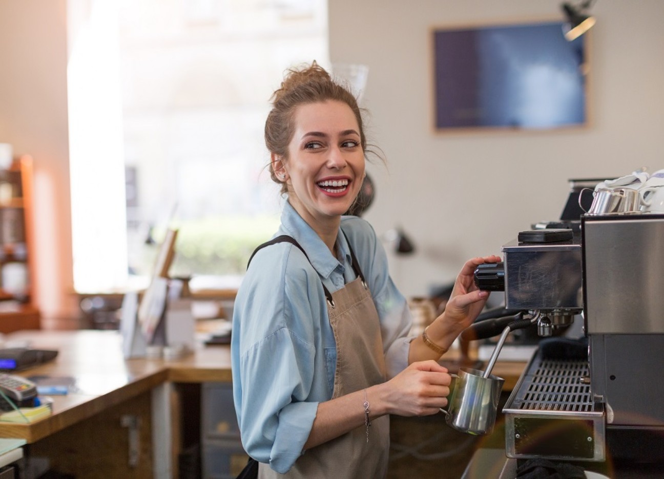Eine junge Frau bereitet als Barista einen Kaffee an einer Kaffeemaschine in einem Café zu. 