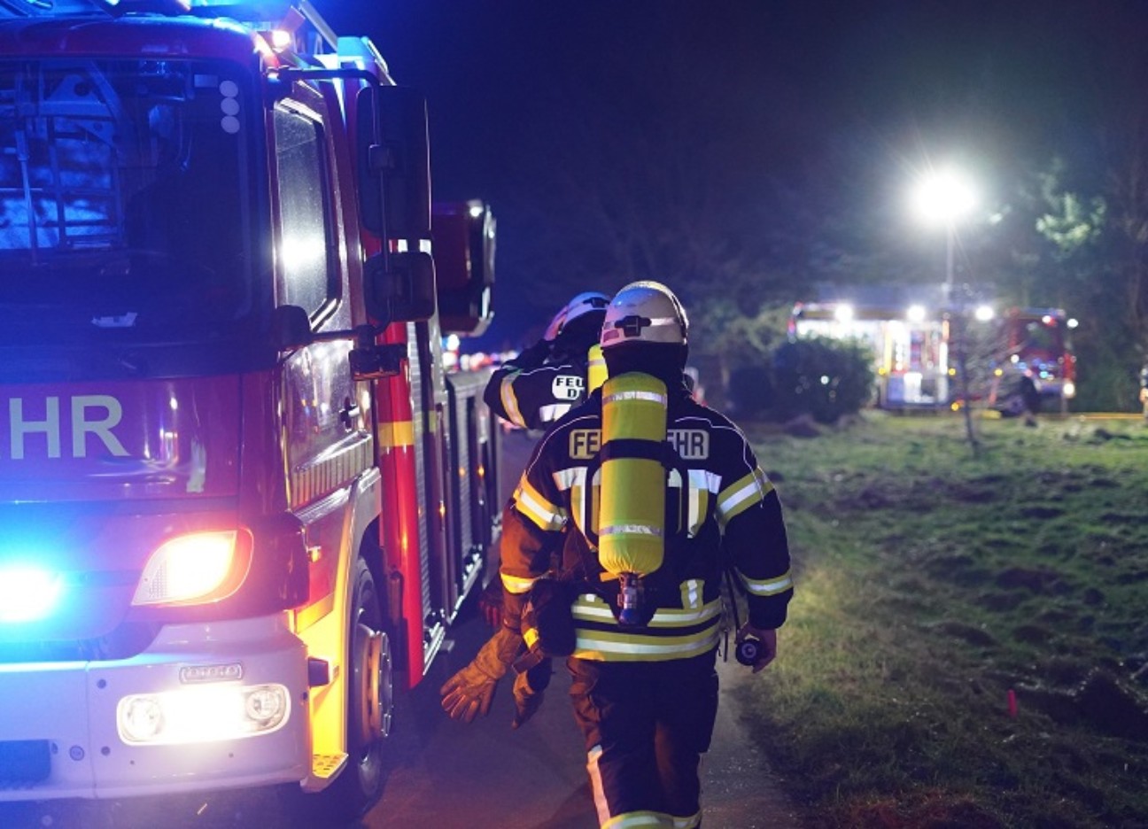 Bühnenbild Ratgeber Unerwartete Ausgaben trotz gesetzlicher Krankenversicherung Feuerwehrmänner gehen entlang Feuerwehrauto zum Einsatz abends.